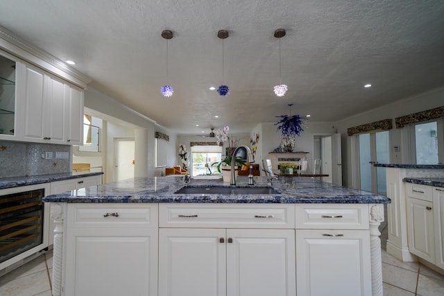 kitchen featuring light tile patterned flooring, beverage cooler, sink, and a center island with sink