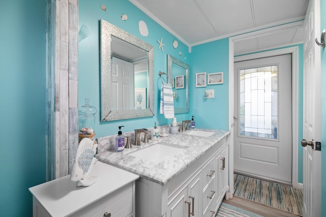 full bath featuring double vanity, wood finished floors, a sink, and crown molding