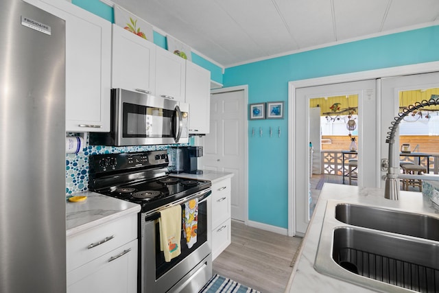 kitchen featuring stainless steel appliances, backsplash, light wood-style flooring, white cabinetry, and a sink