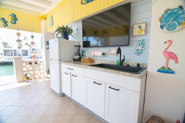 kitchen featuring light stone counters, freestanding refrigerator, white cabinets, light tile patterned flooring, and a sink