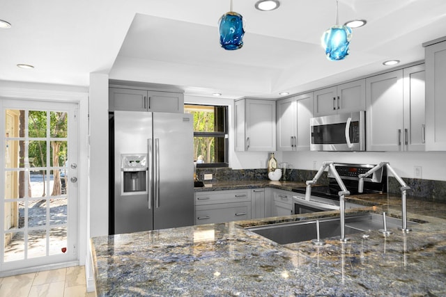 kitchen with stainless steel appliances, gray cabinetry, dark stone countertops, and a healthy amount of sunlight