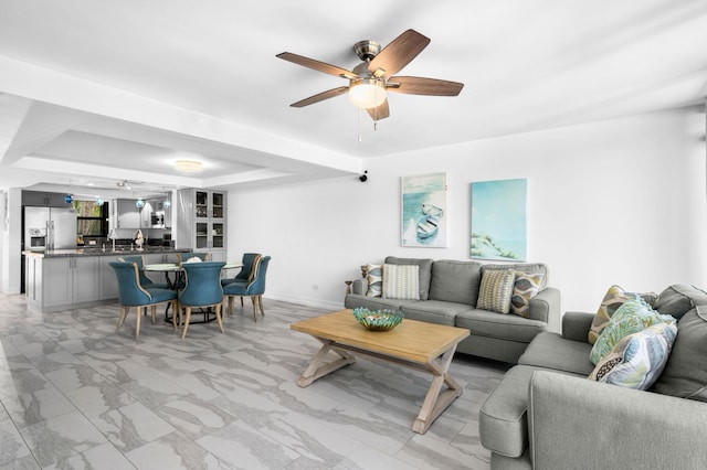 living area featuring marble finish floor, a raised ceiling, a ceiling fan, and baseboards