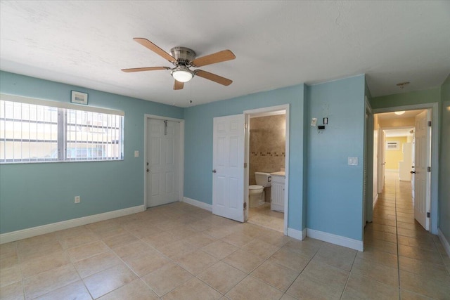 unfurnished bedroom with light tile patterned floors, a ceiling fan, ensuite bathroom, and baseboards