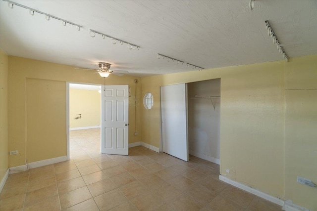 unfurnished bedroom featuring track lighting, ceiling fan, baseboards, light tile patterned flooring, and a closet