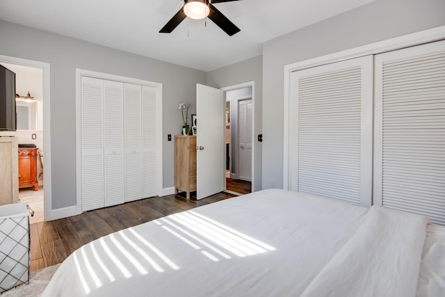 bedroom with a ceiling fan, wood finished floors, baseboards, ensuite bath, and multiple closets