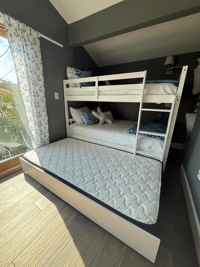 bedroom featuring lofted ceiling with beams, baseboards, and wood finished floors