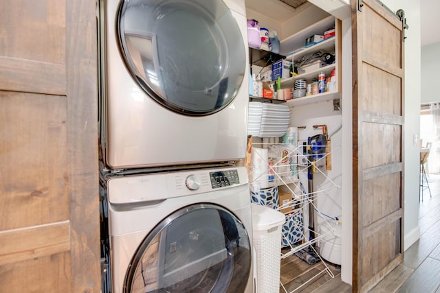 washroom with laundry area, stacked washer and clothes dryer, a barn door, and wood finished floors