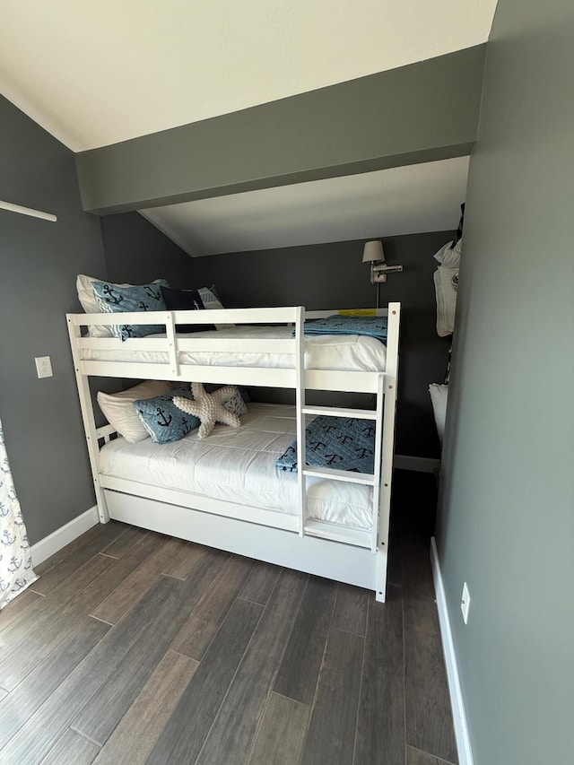 unfurnished bedroom featuring beamed ceiling, baseboards, and wood finished floors