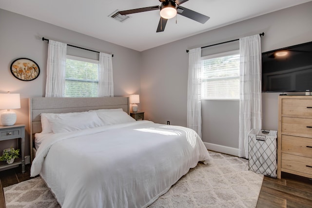 bedroom with ceiling fan, wood finished floors, visible vents, and baseboards