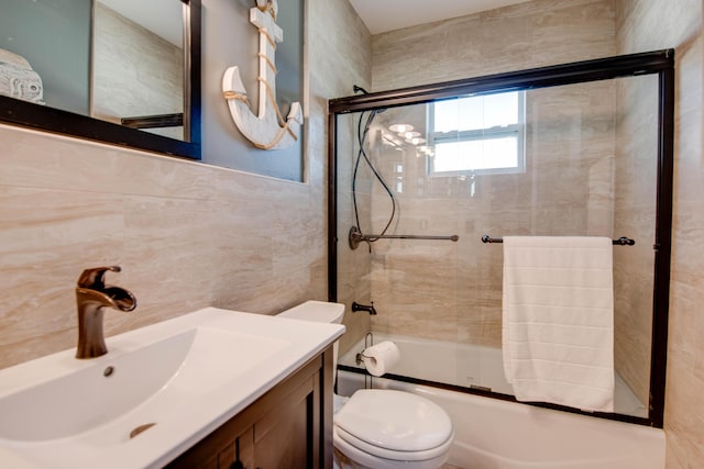 bathroom with combined bath / shower with glass door, toilet, tile walls, and vanity