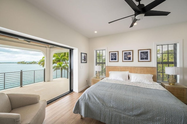 bedroom featuring multiple windows, a water view, access to exterior, and light hardwood / wood-style floors