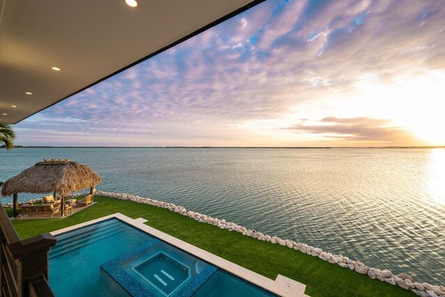 pool at dusk with a gazebo, a water view, a yard, and an in ground hot tub