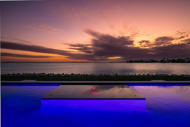 pool at dusk featuring a water view