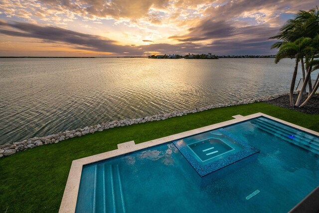 pool at dusk featuring an in ground hot tub, a water view, and a yard