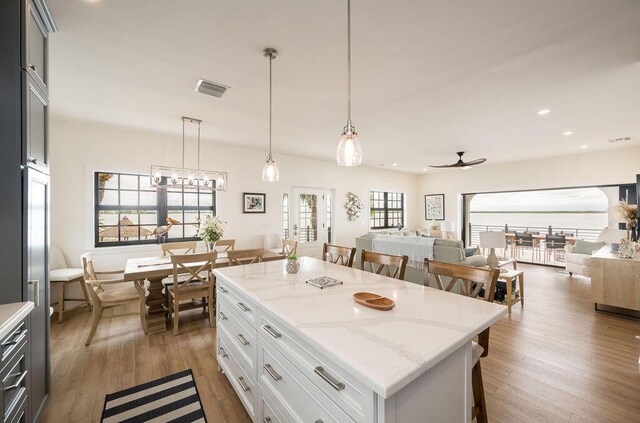 kitchen featuring a breakfast bar, light stone counters, a center island, pendant lighting, and white cabinets