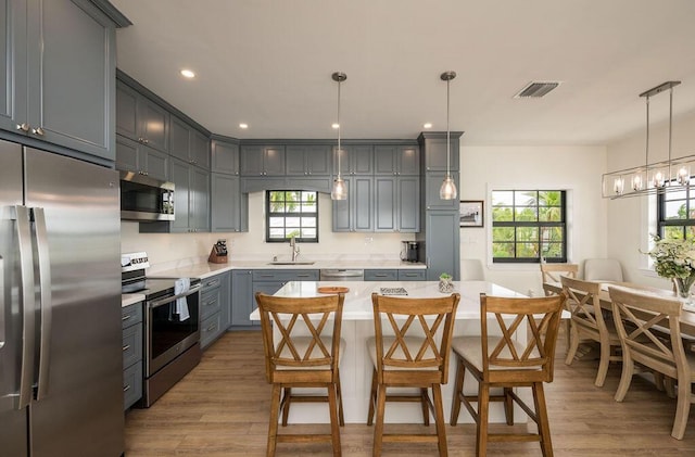 kitchen with gray cabinetry, sink, decorative light fixtures, and stainless steel appliances