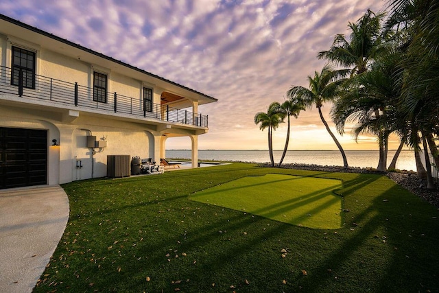 yard at dusk featuring a balcony, a water view, and central AC unit