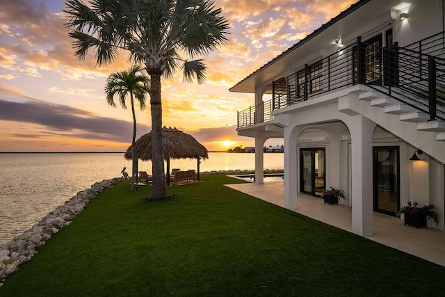 yard at dusk featuring a balcony, a water view, a gazebo, and a patio