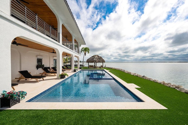 view of pool with a yard, a patio area, ceiling fan, and a water view