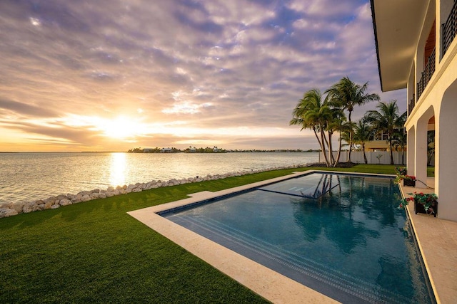 pool at dusk featuring a yard and a water view