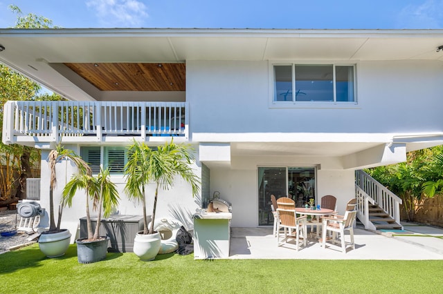 rear view of property with a patio area, stucco siding, a lawn, and a balcony