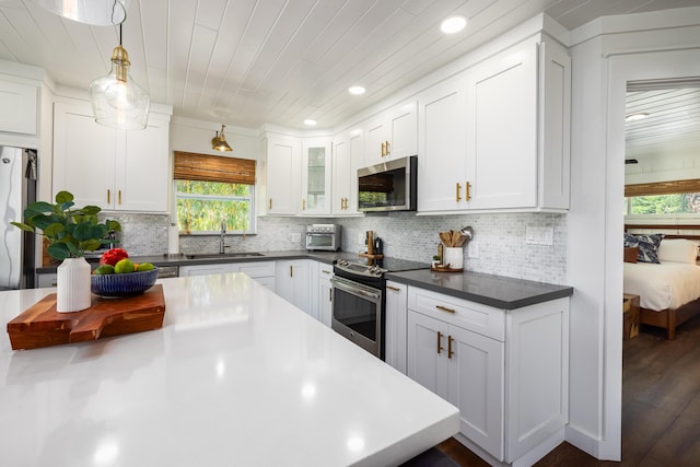 kitchen featuring tasteful backsplash, stainless steel appliances, dark countertops, and a sink