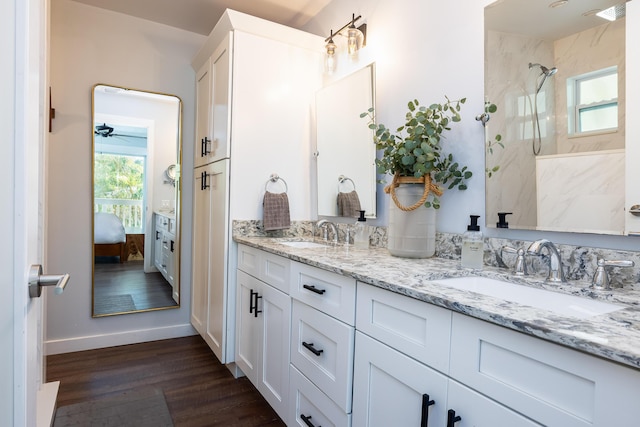 ensuite bathroom with a marble finish shower, double vanity, wood finished floors, and a sink