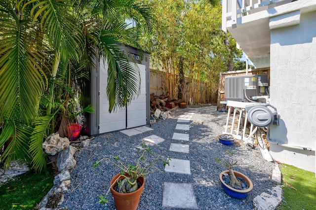 view of yard featuring a shed, an outdoor structure, a balcony, central AC unit, and fence private yard