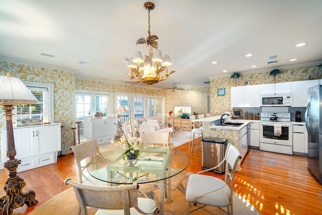 dining area featuring crown molding, sink, a chandelier, and light wood-type flooring