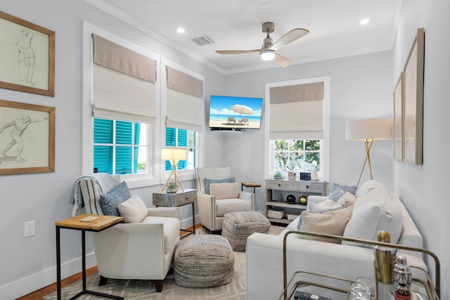 living area featuring wood finished floors, visible vents, baseboards, ceiling fan, and ornamental molding