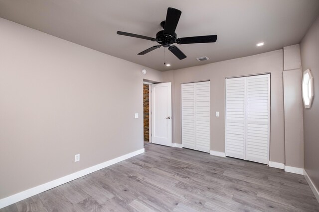 unfurnished bedroom featuring ceiling fan, two closets, and light wood-type flooring