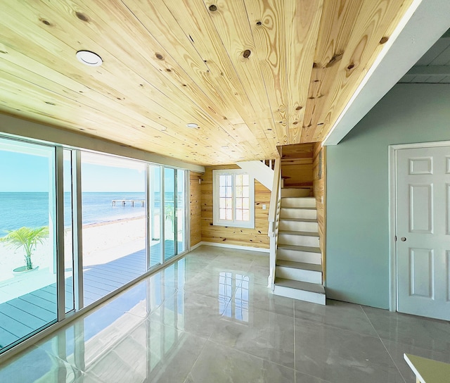 interior space with a water view, wood ceiling, a view of the beach, and wood walls