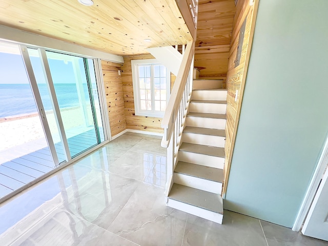 stairway with a water view, wood ceiling, a view of the beach, and wood walls