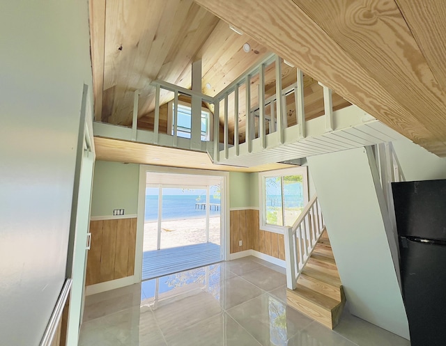 interior space with vaulted ceiling, wood walls, a water view, wooden ceiling, and tile patterned floors