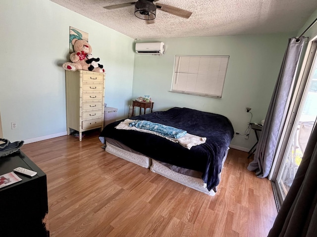 bedroom featuring ceiling fan, a textured ceiling, light hardwood / wood-style floors, and a wall mounted AC