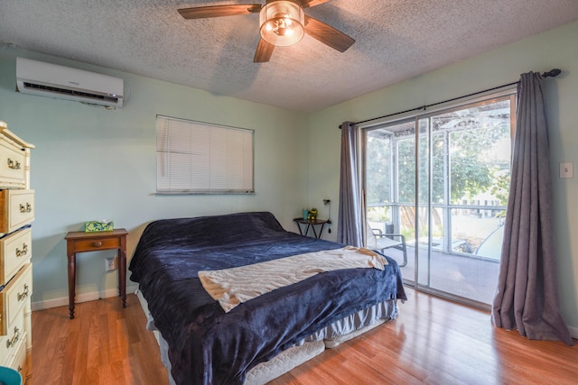 bedroom with an AC wall unit, access to exterior, ceiling fan, a textured ceiling, and light hardwood / wood-style flooring