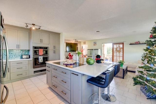 kitchen featuring a kitchen island, appliances with stainless steel finishes, a breakfast bar area, gray cabinetry, and light tile patterned floors