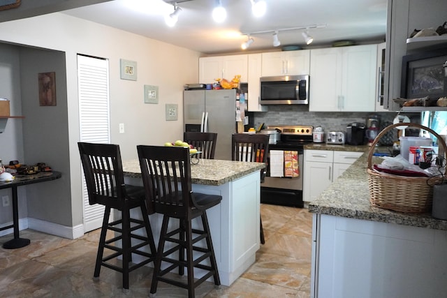 kitchen with white cabinetry, a kitchen bar, decorative backsplash, and appliances with stainless steel finishes