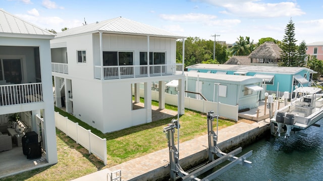rear view of property with boat lift, a water view, metal roof, fence, and a standing seam roof