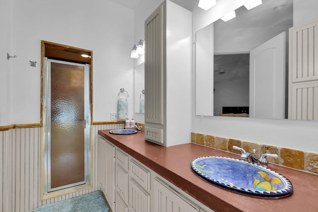 full bathroom with wainscoting, a sink, a shower stall, and double vanity