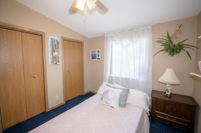 bedroom featuring two closets, vaulted ceiling, ceiling fan, and dark colored carpet