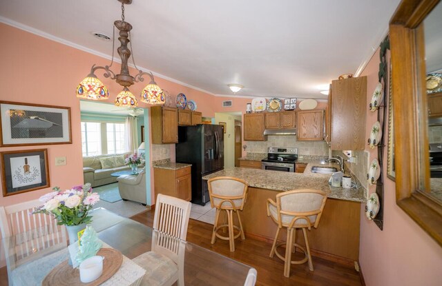 kitchen with a kitchen bar, black fridge, decorative light fixtures, kitchen peninsula, and stainless steel electric stove