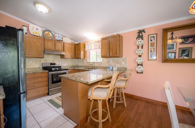 kitchen with a breakfast bar, sink, stainless steel range with electric cooktop, kitchen peninsula, and black fridge