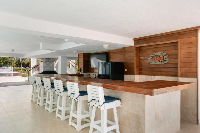 kitchen with black refrigerator, a textured ceiling, a breakfast bar, and kitchen peninsula