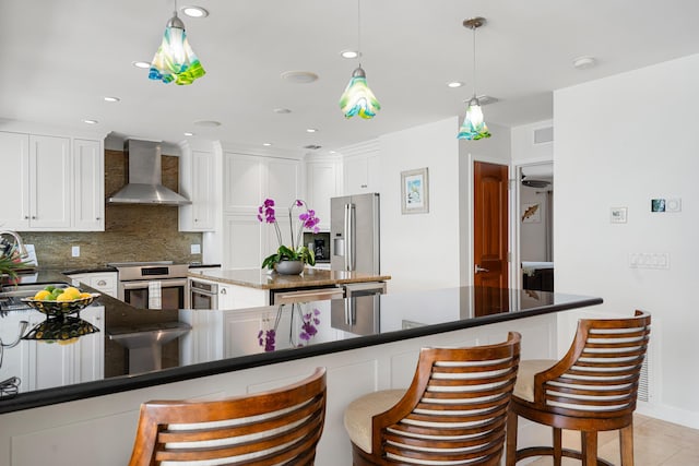 kitchen with pendant lighting, wall chimney range hood, stainless steel appliances, tasteful backsplash, and white cabinets