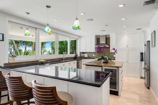 kitchen featuring sink, hanging light fixtures, stainless steel appliances, white cabinets, and wall chimney exhaust hood