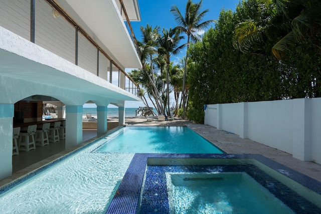 view of swimming pool featuring an in ground hot tub, a water view, and a patio area