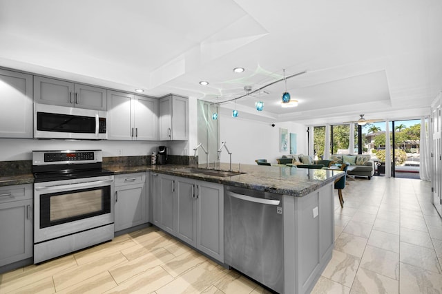 kitchen featuring sink, gray cabinetry, stainless steel appliances, a raised ceiling, and kitchen peninsula