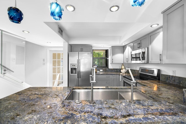 kitchen with gray cabinets, dark stone countertops, appliances with stainless steel finishes, and pendant lighting