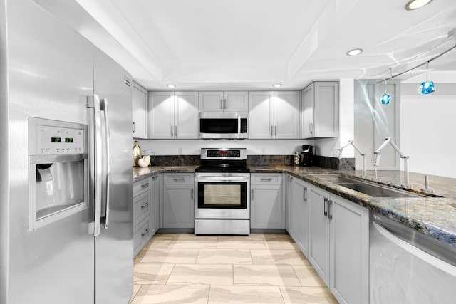 kitchen with sink, gray cabinetry, dark stone countertops, a tray ceiling, and stainless steel appliances